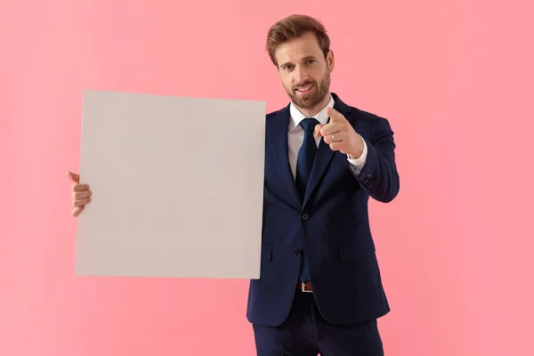 Självsäker affärsman som håller en tom skylt och pekar på — Stockfoto