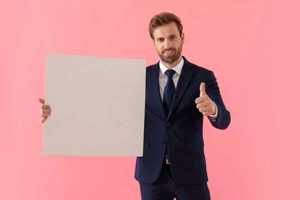 Positieve zakenman die een leeg reclamebord vasthoudt en duimen geeft — Stockfoto