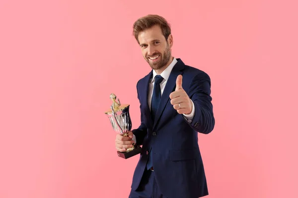 Happy businessman holding his trophy and giving a thumbs up — Stock Photo, Image