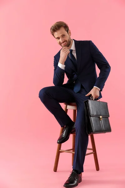 Affascinante uomo d'affari in possesso di una valigetta e mano sul mento — Foto Stock