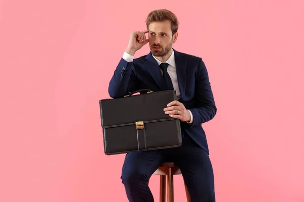 Hombre de negocios pensativo sosteniendo un maletín y la mano en la frente —  Fotos de Stock