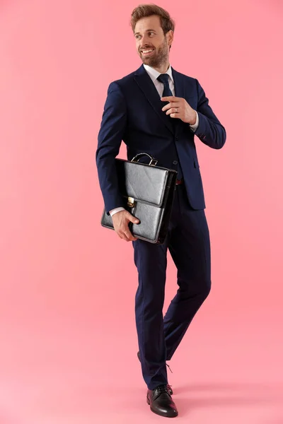 Vrolijke zakenman die een aktetas vasthoudt en zijn das aanpast — Stockfoto