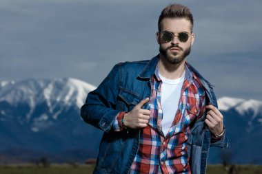 Havalı adam güneş gözlüğü takarken ceketini düzeltiyor.