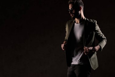 Tıraşsız seksi genç manken moda ışığında ceketini ayarlıyor.