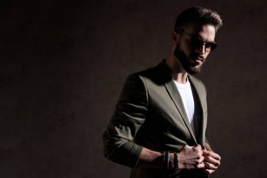 Havalı, tıraşsız, yeşil ceketi tamir eden ve taraf arayan adam.