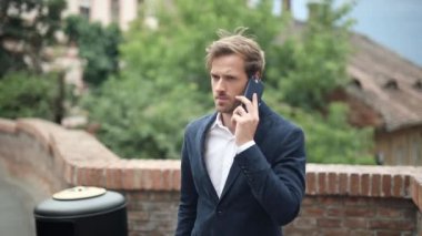 Endişeli ve ciddi zeki sıradan bir adam şehrin caddesinde telefonla konuşuyor.