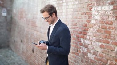 Gözlüklü genç adam telefonuyla kitap okuyor ve kahve içerken yürümeye başlıyor.