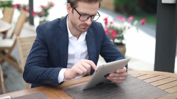 Mladý inteligentní ležérní muž sedí u stolu v restauraci a pracuje na svém tabletu počítače — Stock video