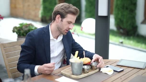 Νεαρός άνδρας τρώει ένα burger με πιρούνι και μαχαίρι σε ένα εστιατόριο μπιστρό — Αρχείο Βίντεο