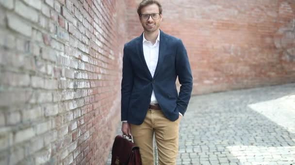 Camera moving in a smart casual man holding suitcase and wearing glasses with hand in pocket — Stock Video