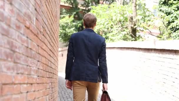 Vista trasera de un joven hombre casual inteligente caminando con su maleta girando y saludando con apretón de manos — Vídeos de Stock