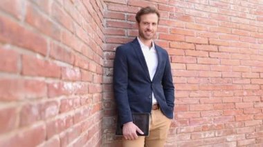 Tablet tutan ve tasmasını düzelten gülümseyen genç adam, kamera ona doğru geliyor.