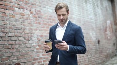 Genç, akıllı, sıradan bir adam telefonundan ilginç haberler okurken kahvesini içiyor.