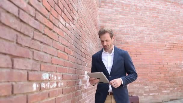 Glimlachende slimme casual man lopen en werken op zijn tablet wijst vinger naar de camera — Stockvideo