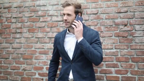 Ευτυχισμένος νεαρός έξυπνος, χαλαρός άντρας, απαντάει στο τηλέφωνο, μιλάει και μετά βάζει το τηλέφωνό του στην εσωτερική τσέπη του παλτού του. — Αρχείο Βίντεο