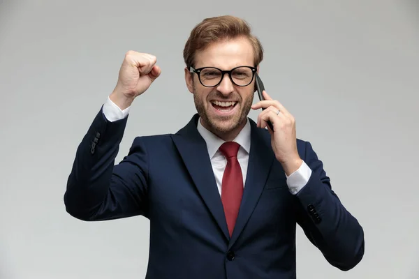 Businessman standing with one fist raised while talking on phone — Stockfoto
