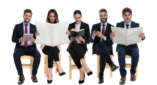 5 businessmen reading from book, newspapers, tablet and phone — Stockfoto