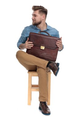 smiling young guy holding suitcase and looking to side