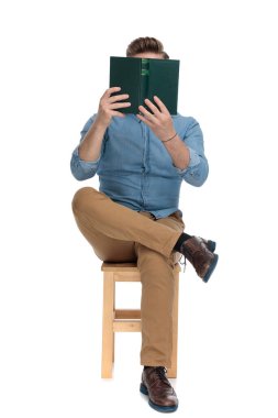 young casual man covering face with book and reading
