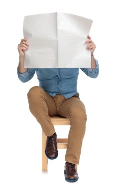casual young man in denim shirt hiding behind newspaper