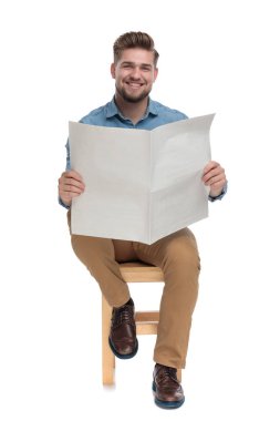 young casual man reading newspaper and smiling