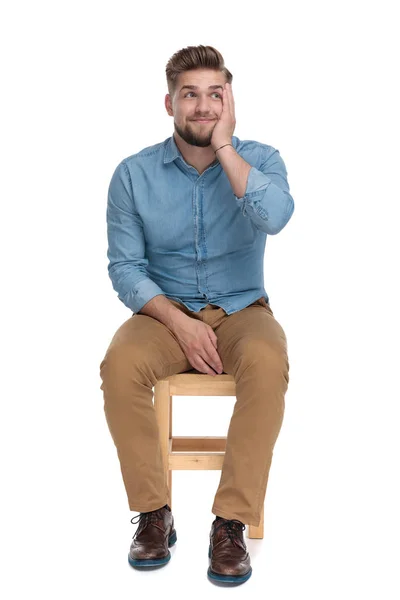 Happy young guy in denim shirt holding hand to face and smiling — Stock Photo, Image