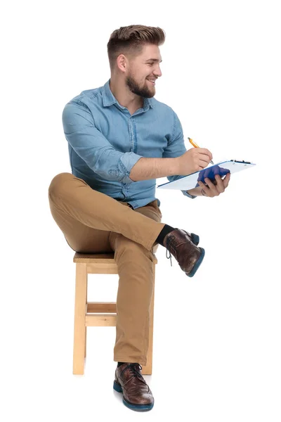 Young casual man smiling and writing on clipboard — 图库照片
