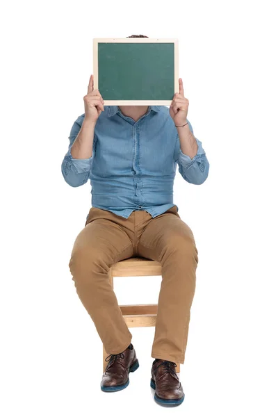 Young casual man covering face with empty blackboard — Stockfoto
