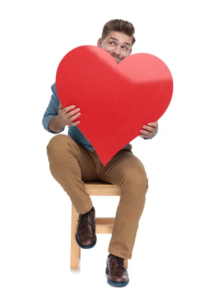 Giovane uomo casual guardando in su e tenendo grande cuore rosso — Foto Stock
