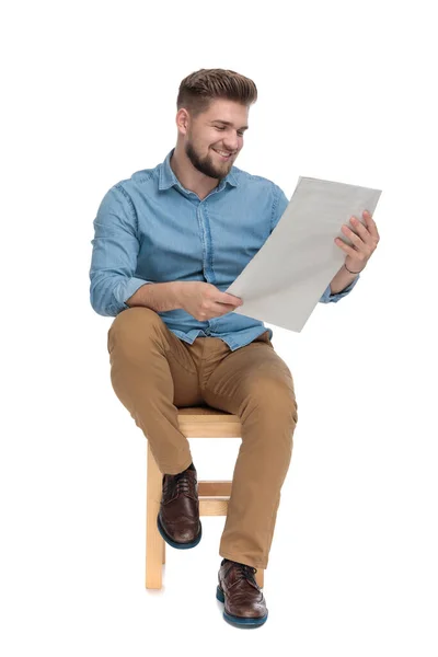 Happy young man smiling and reading newspaper — 图库照片