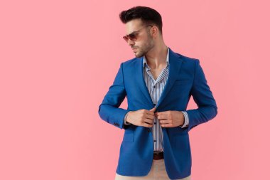 sexy young smart casual guy adjusting coat and looking to side