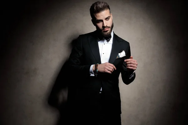 Confident elegant guy in tuxedo adjusting coat — Stock Photo, Image