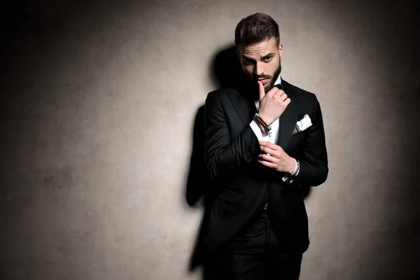 Sexy elegante hombre en esmoquin tocando los labios en una pose de moda — Foto de Stock