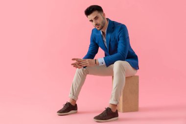 sexy young man holding elbows on knees in a fashion pose