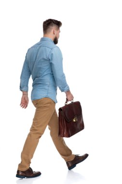 Elinde evrak çantası olan ve beyaz stüdyo arka planında yürüyen motivasyonlu sıradan bir adamın yan görüntüsü.