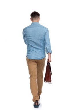 Elinde evrak çantası olan ve beyaz stüdyo arka planında yürüyen kararlı bir adamın arka görüntüsü.