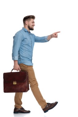 Evrak çantasını tutan ve beyaz stüdyo arka planına basan neşeli bir adamın yan görüntüsü.