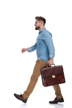 Elinde evrak çantası olan ve beyaz stüdyo arka planında yürüyen neşeli bir adamın yan görüntüsü.