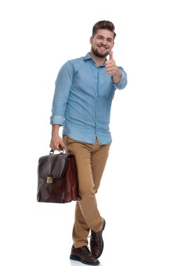 Neşeli sıradan adam el kol hareketi yapıyor. Tamam, evrak çantasını tutarken gülüyor ve beyaz stüdyo arka planında duruyor.