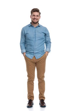 Beyaz stüdyo arka planında dururken iki eli cebinde gülen sıradan bir adam.