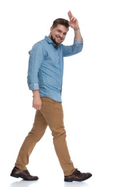 Beyaz stüdyo arka planında yürürken gülen ve selamlaşan mutlu bir adamın yan görüntüsü