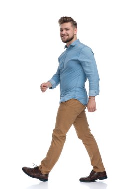 Beyaz stüdyo arka planında yürüyen kendinden emin sıradan bir adamın yan görüntüsü.