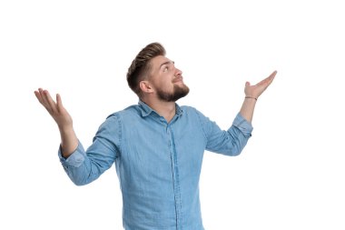 Genç, sıradan bir adam, gömlek giyerken, beyaz stüdyo arka planında dikilirken bilmediğine dair işaretler yapıyor.