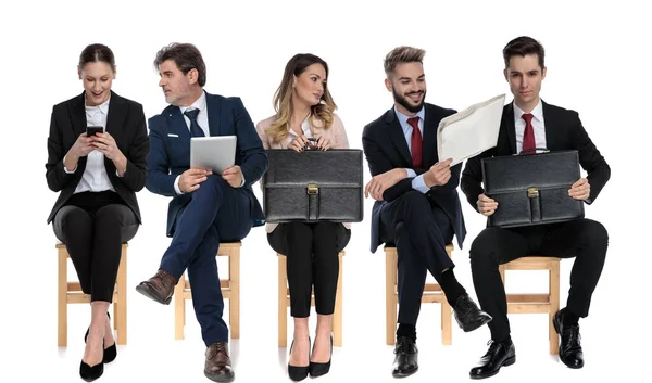 ホワイトスタジオの背景にある椅子に座って面接を待っている間に 5人のビジネスマンのチームが電話 タブレット ブリーフケースを持っています — ストック写真
