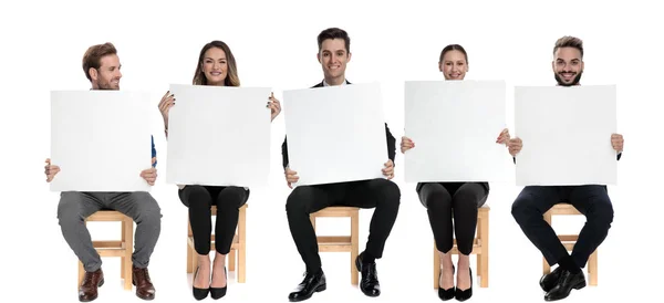 白いスタジオの背景に椅子に座っている間に空の看板を保持している5幸せなビジネスマンのチーム — ストック写真
