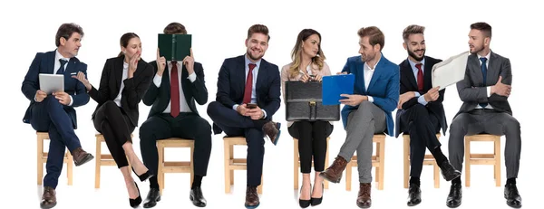 由8名商人组成的团队在等待求职面试时 坐在白色工作室背景的椅子上 一边读书一边聊天 — 图库照片