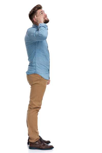 Side view of a casual man pointing to his head and looking up, standing on white studio background