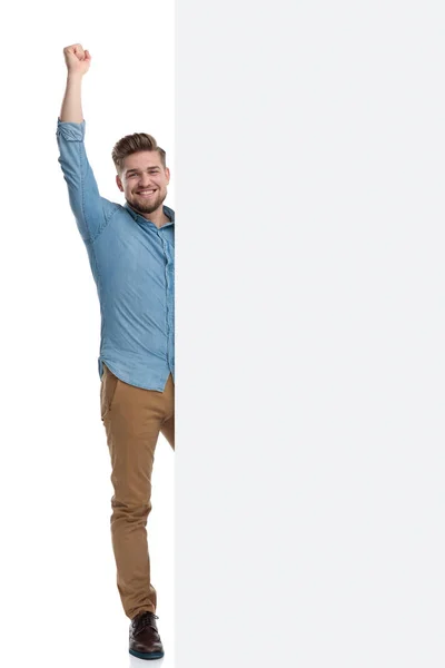 站在白人摄影棚的背景下 手握拳头 站在一块空白的广告牌后面 欢快地庆祝着 — 图库照片