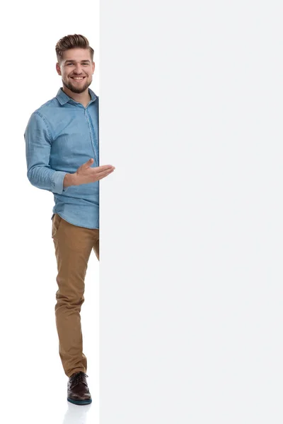 白いスタジオの背景に立っている間に若いカジュアルな男は笑顔と空白の看板を提示 — ストック写真