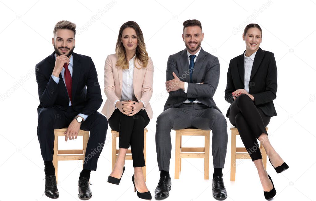 Team of 4 positive businessmen smiling while sitting on chairs on white studio background